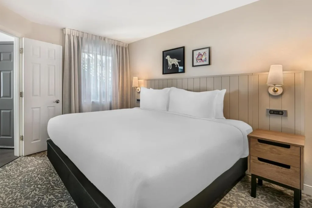 Dormitorio con una cama king y mesita de noche de madera en Sonesta ES Suites Lake Buena Vista