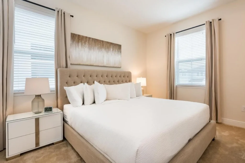 Bedroom with a large bed, tufted headboard and two windows in an Encore Resort home