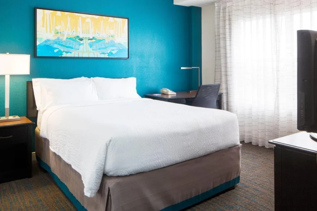 Dormitorio con una cama, pared de cerceta, obras de arte y un pequeño escritorio en el Residence Inn Orlando at SeaWorld