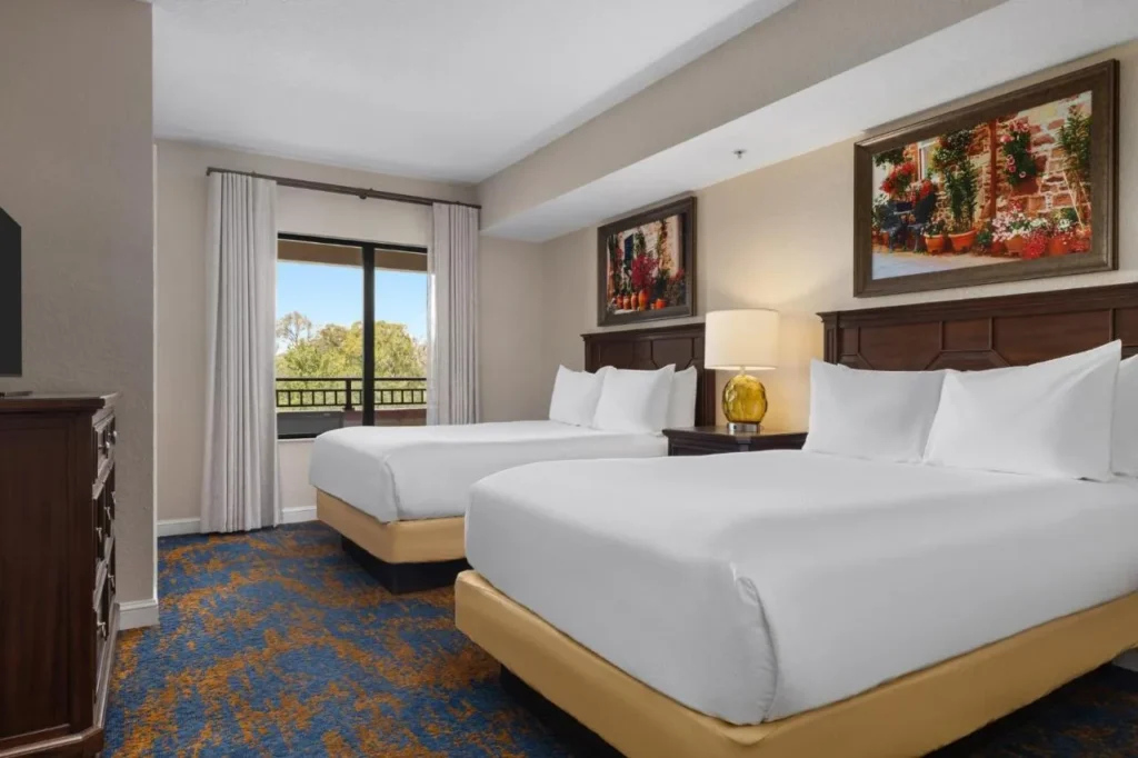 Dormitorio con dos camas, arte floral enmarcado y una puerta de balc&oacute;n en Club Wyndham Bonnet Creek