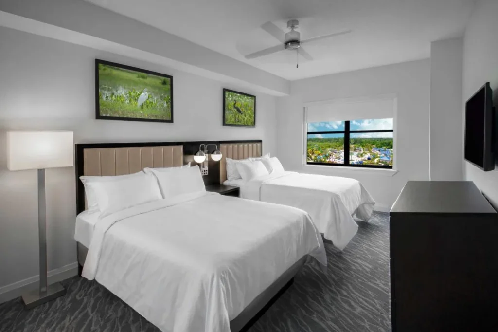 Dormitorio con dos camas queen y una ventana sobre las piscinas en el Grove Resort