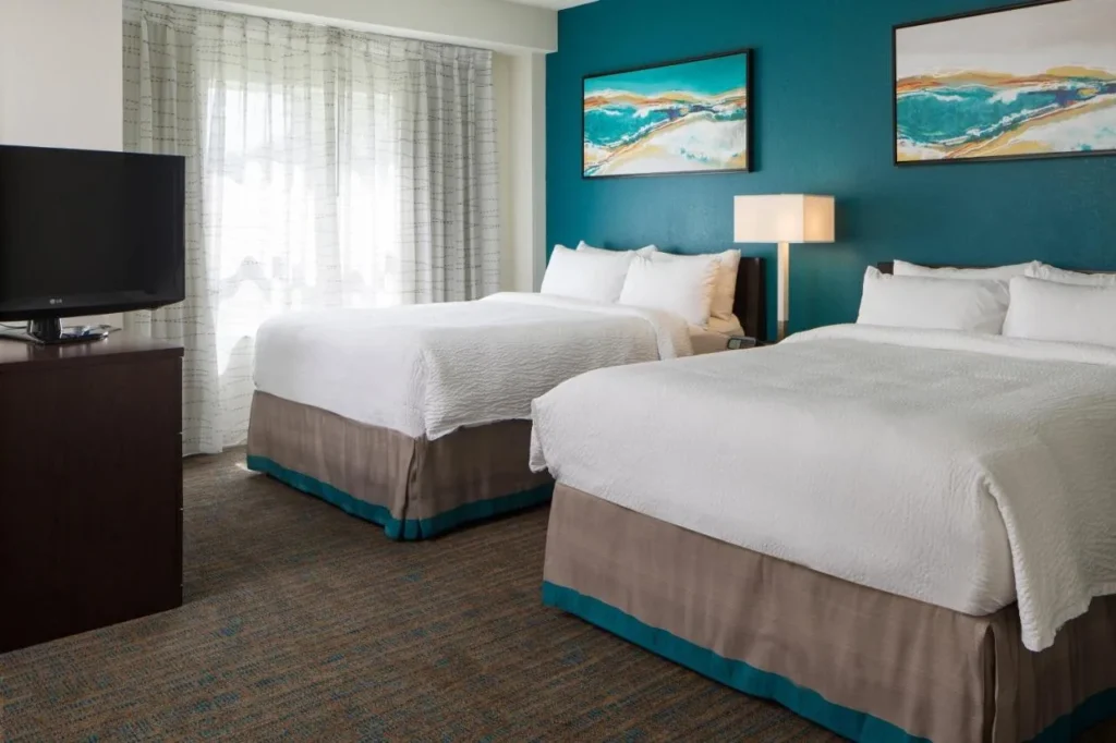 Dormitorio con dos camas queen, pared de acento verde azulado y arte de la ola en el Residence Inn SeaWorld