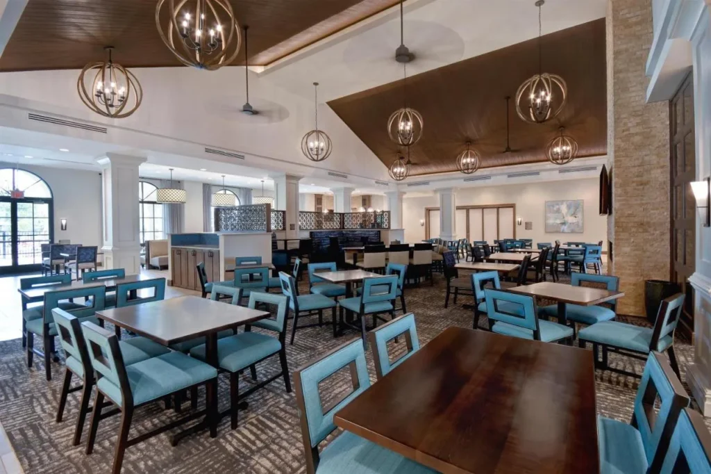 Breakfast room with blue chairs and wood tables under chandeliers at Homewood Suites Flamingo Crossings