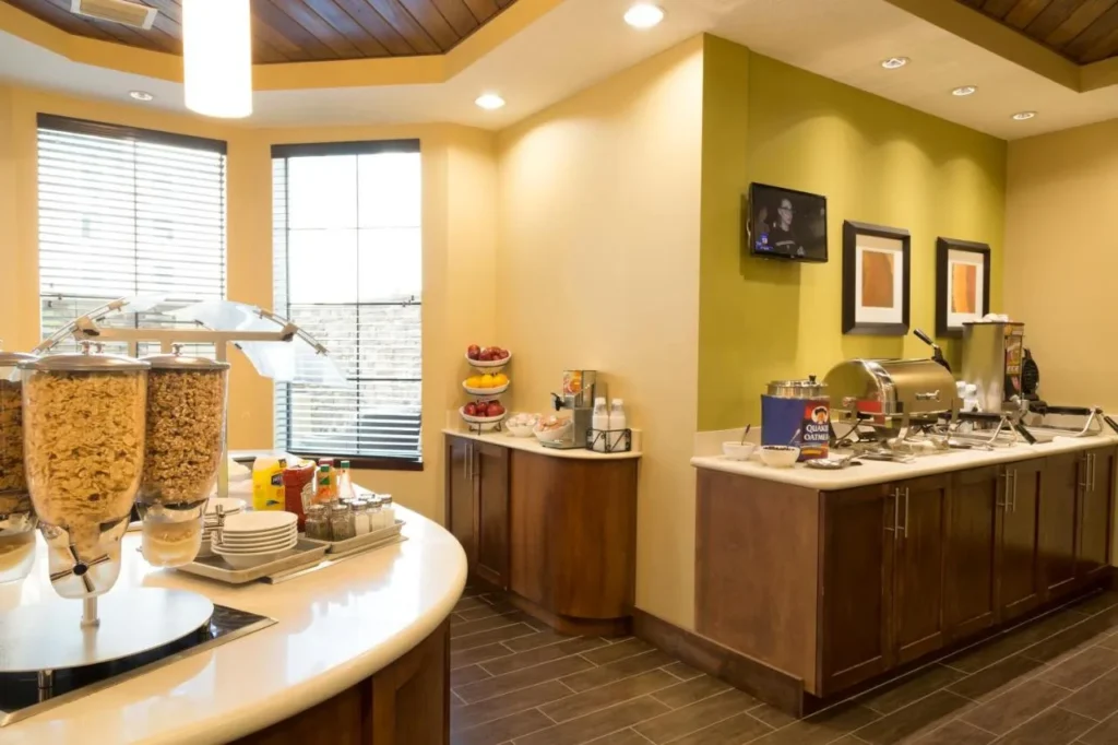 Sala de desayunos con dispensadores de cereales, fruta y mostrador de comida caliente en Staybridge Suites Orlando at SeaWorld
