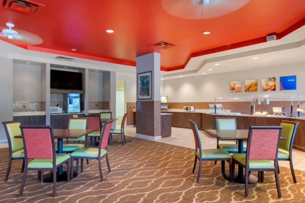 Sala de desayunos con techo rojo, sillas coloridas y l&iacute;nea de buffet en Comfort Suites Maingate East