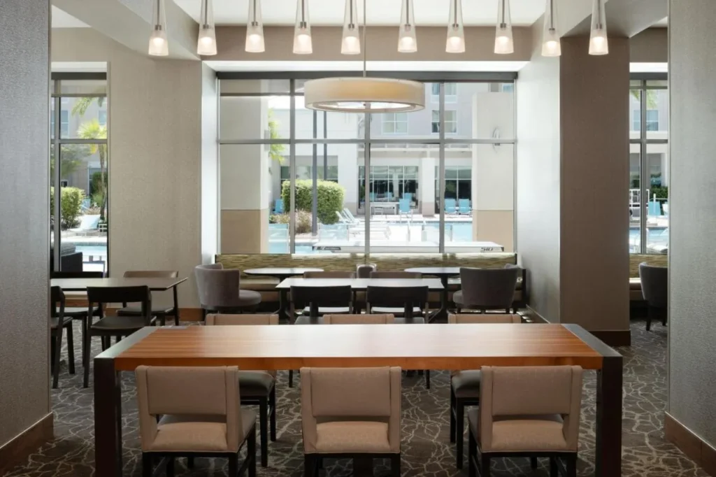 Asientos para el desayuno con mesas de madera y ventanas frente a la piscina en SpringHill Suites Flamingo Crossings