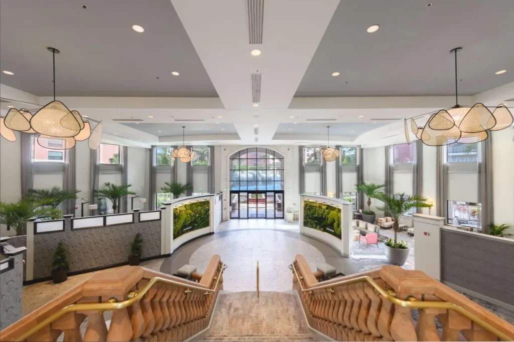 Luminoso vest&iacute;bulo de recepci&oacute;n Caribe Royale Orlando con una gran escalera, plantas y luces colgantes de rat&aacute;n