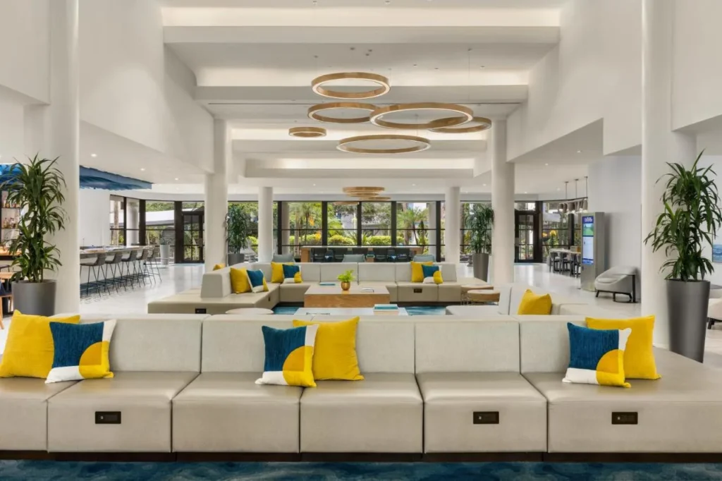 Sal&oacute;n luminoso en el vest&iacute;bulo con sof&aacute;s largos y cojines amarillos en Delta Hotels Orlando Celebration