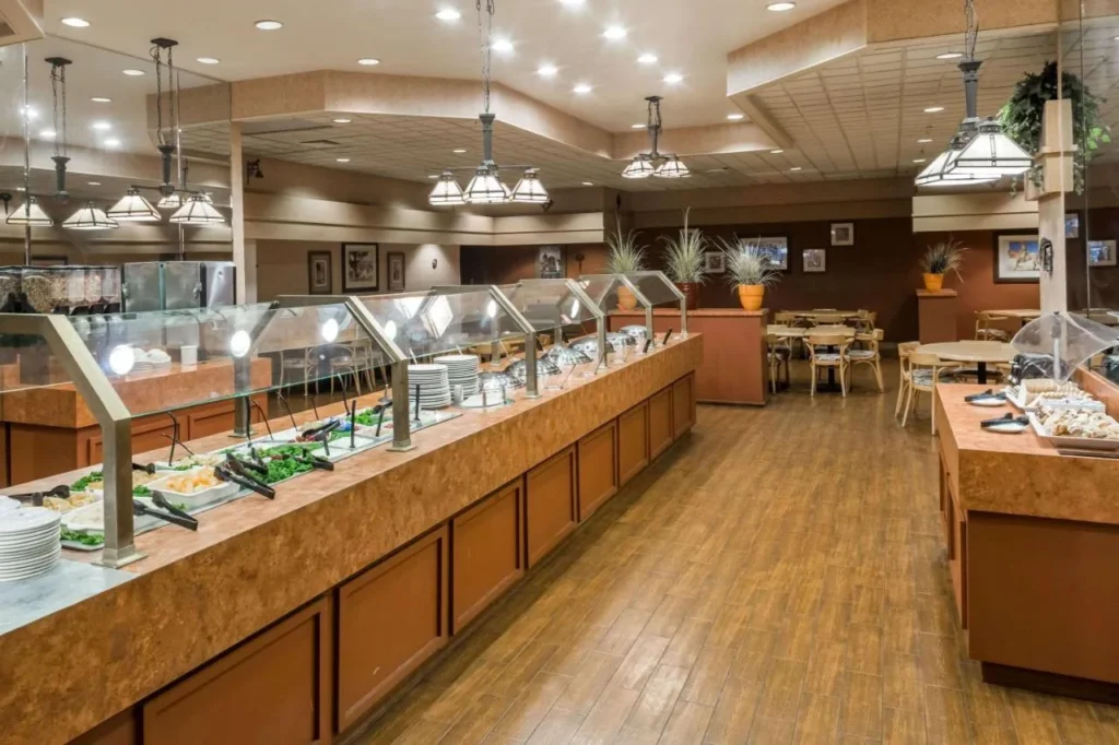 Restaurante buffet con mostradores de servicio prolongado y mesas de comedor en Ramada by Wyndham Kissimmee Gateway