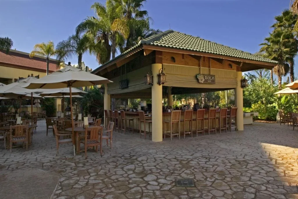 Bula Bar junto a la piscina con mesas al aire libre bajo las palmeras en Loews Royal Pacific Resort