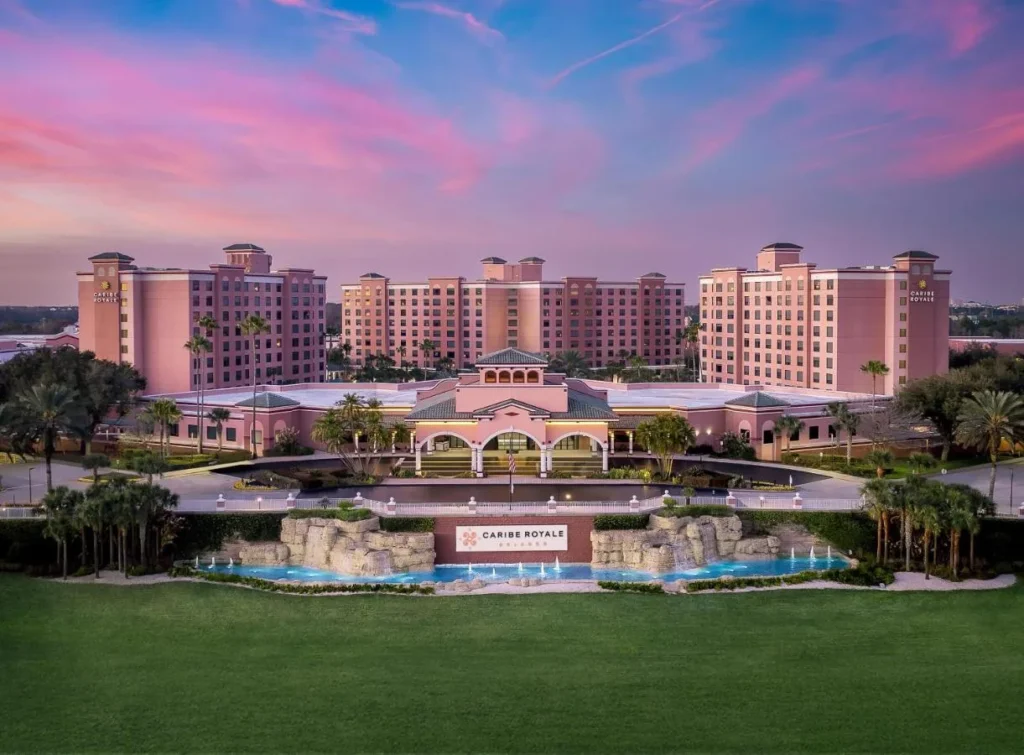 Las tres torres rosas de Caribe Royale Orlando, el edificio de recepci&oacute;n y las fuentes de entrada al atardecer
