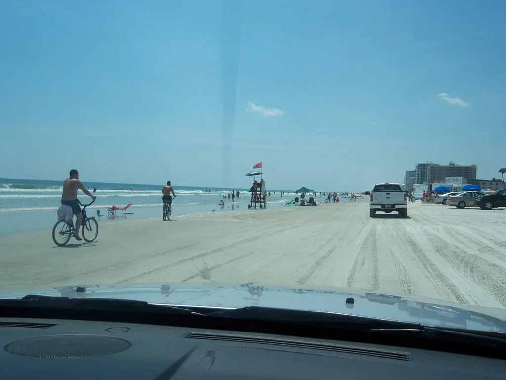 Coches y ciclistas en la arena en Daytona Beach junto a un puesto de salvavidas