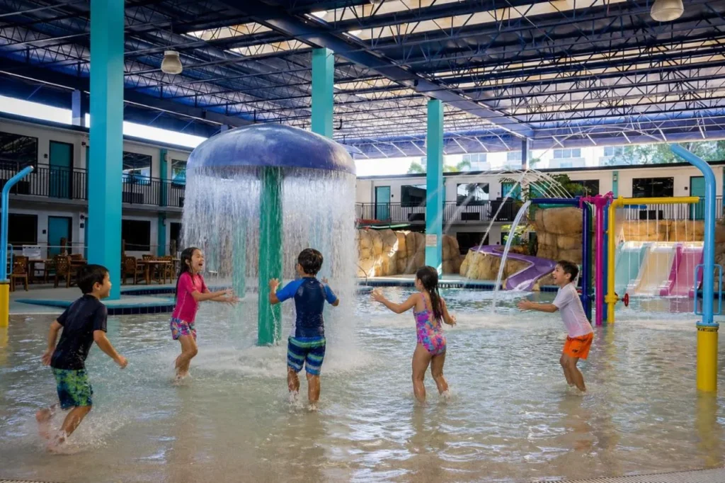 Ni&ntilde;os jugando bajo una fuente de hongos en el &aacute;rea cubierta de salpicaduras en CoCo Key Water Resort