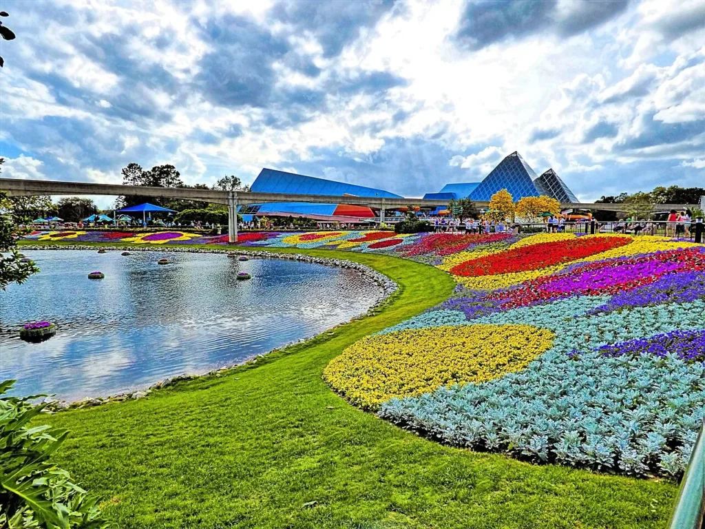 Colorful festival flower beds beside a lagoon at EPCOT, below the monorail beam and Imagination pyramids