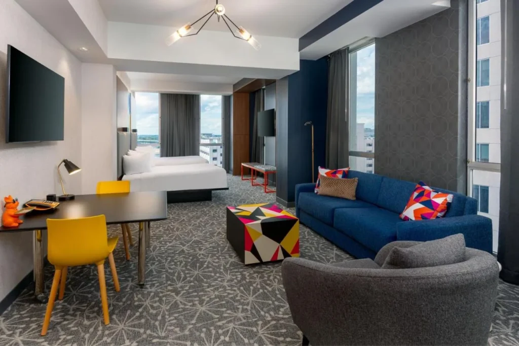 Suite colorida con sof&aacute; azul, sillas amarillas y dos camas en el Aloft Orlando Downtown