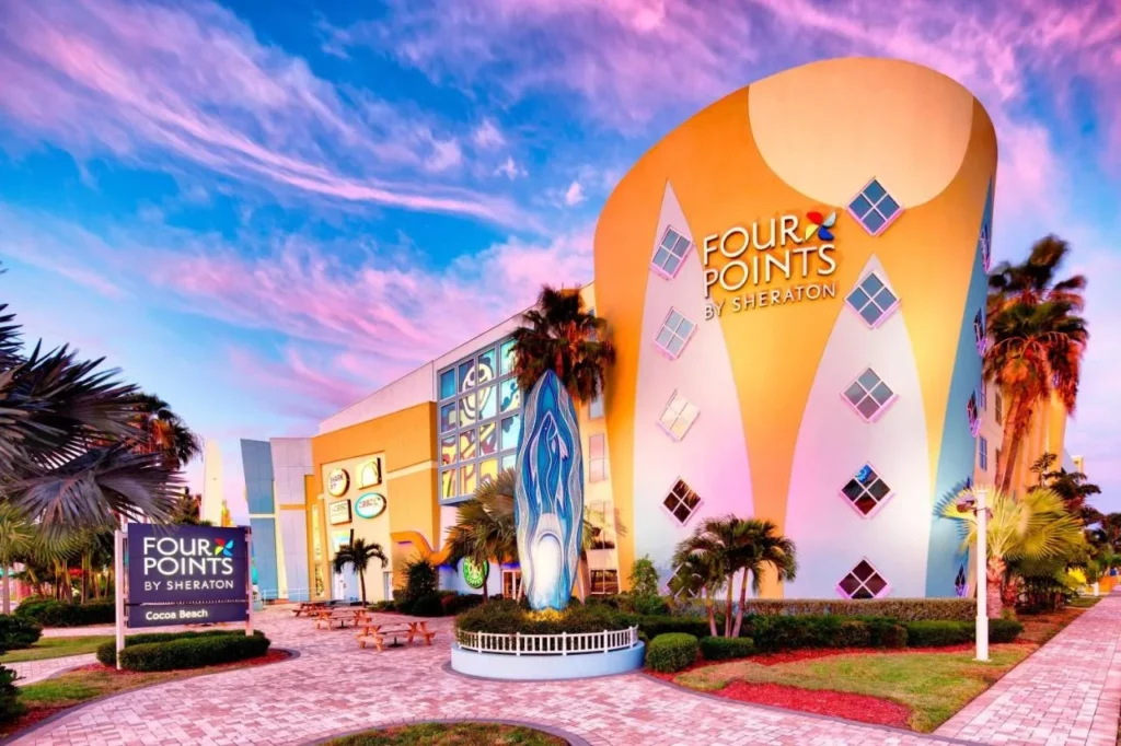 Colorful surf-themed facade and entrance of Four Points by Sheraton Cocoa Beach under a pink sky