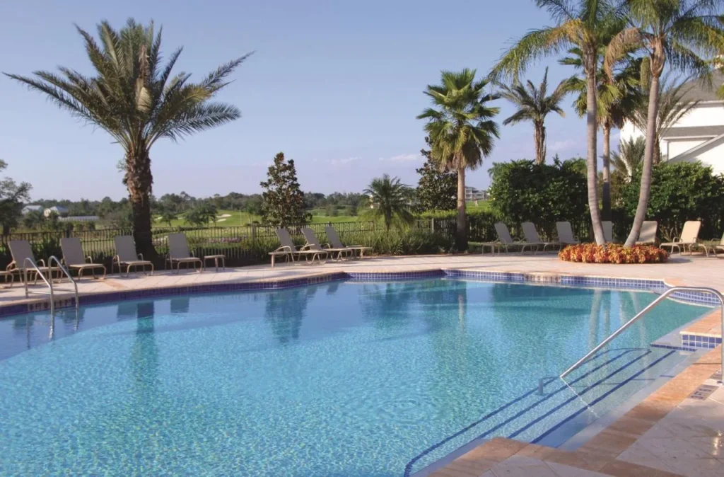 Community pool with lounge chairs and palm trees beside the golf course at Reunion Resort