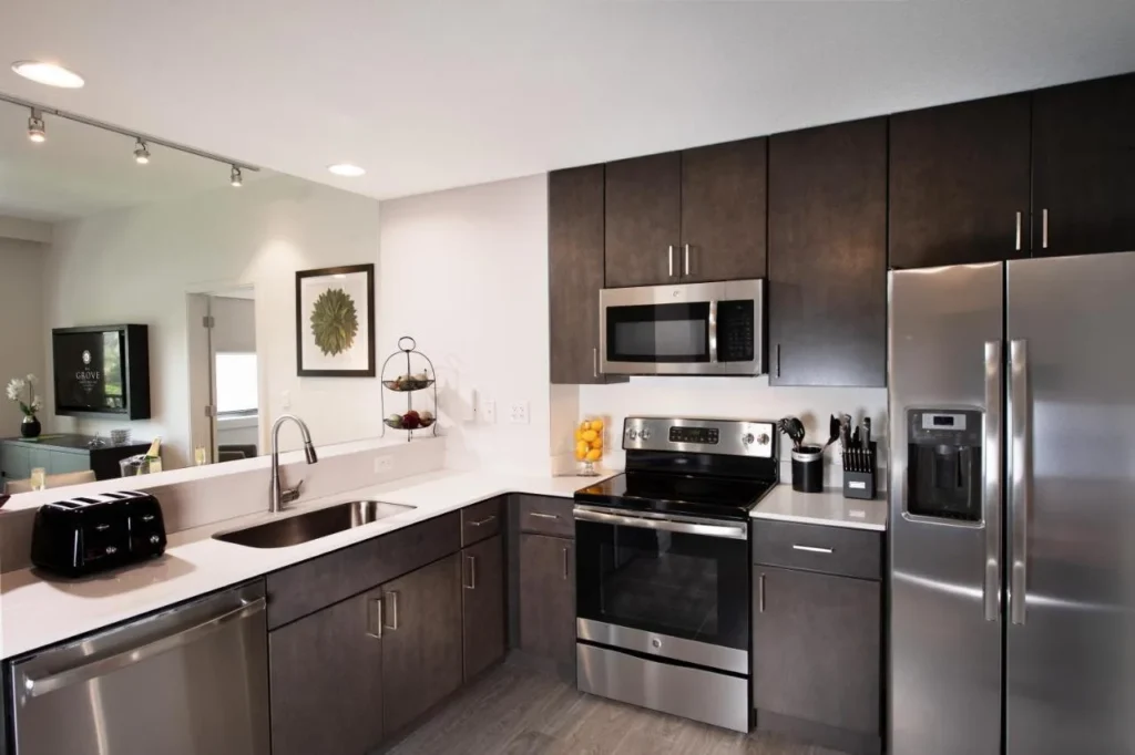 Cocina de condominio con gabinetes oscuros, electrodom&eacute;sticos de acero inoxidable y un mostrador de desayuno en The Grove Resort Orlando