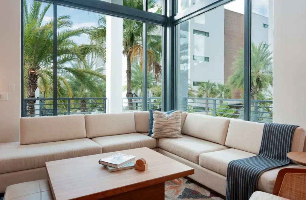 Corner sectional sofa below double-height windows framing palm trees at Evermore Orlando Resort