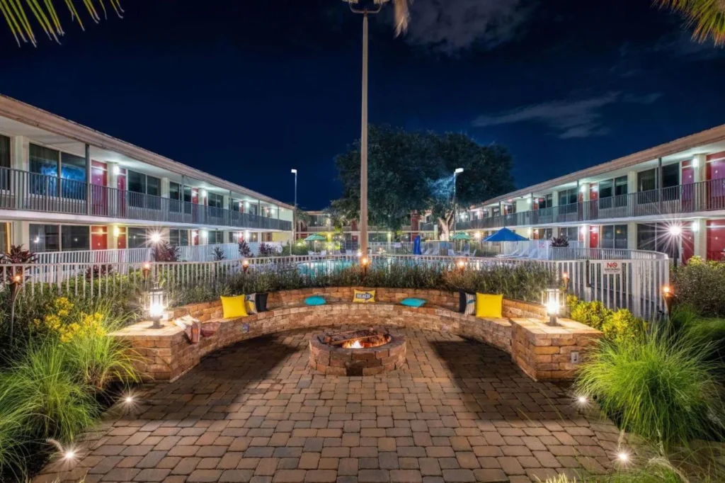 Courtyard fire pit with stone seating between two-story room wings at night at Ramada Kissimmee Gateway