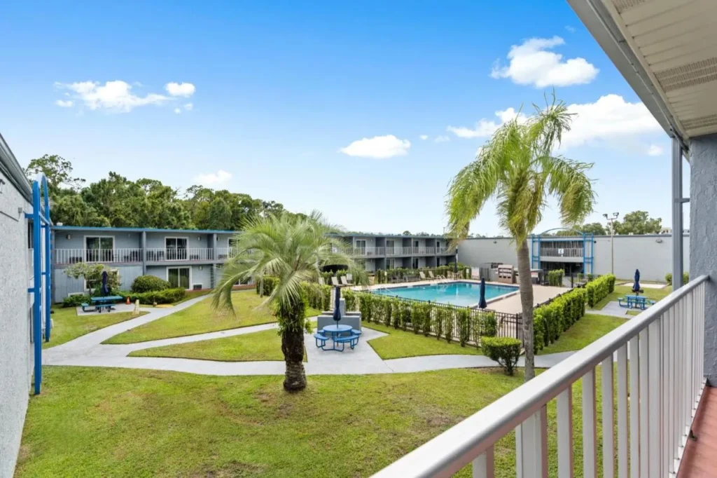 Courtyard con césped, palmeras y piscina al aire libre visto desde una pasarela superior en Celebration Suites