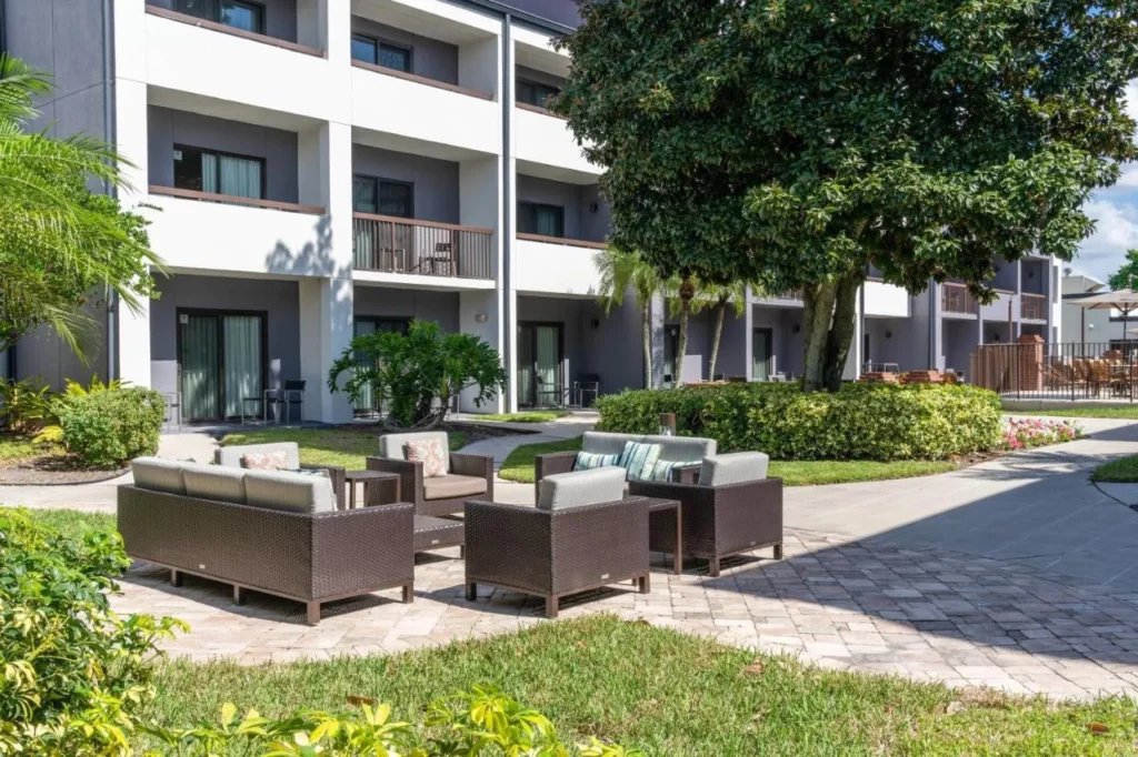 Courtyard con sof&aacute;s de mimbre, &aacute;rbol de sombra y balcones en Courtyard by Marriott Orlando Airport