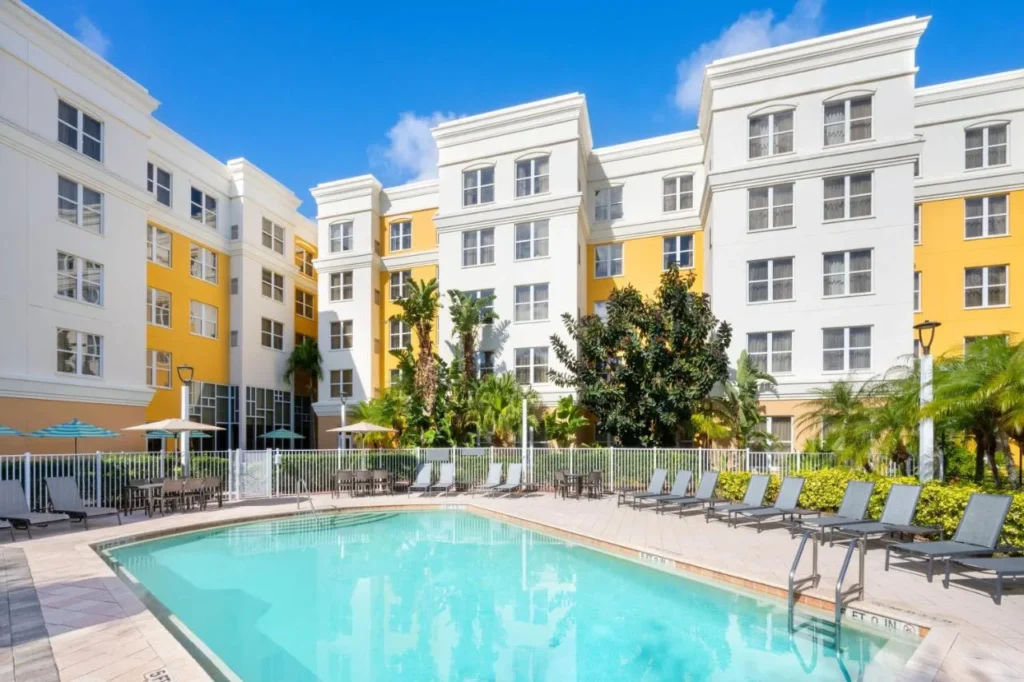 Piscina en el Courtyard con tumbonas junto a los edificios blancos y amarillos del Residence Inn Daytona Beach Speedway/Airport