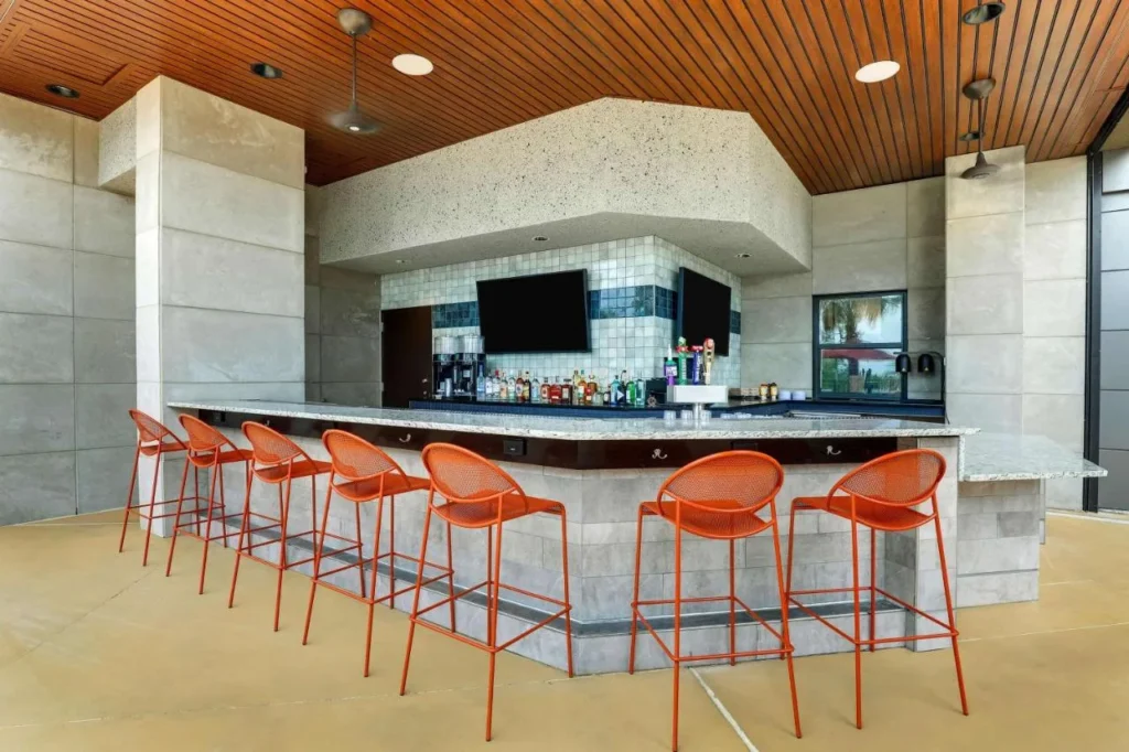 Bar al aire libre cubierto con taburetes naranjas, televisores y un mostrador de piedra en Drury Plaza Hotel Orlando