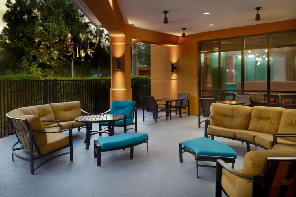 Covered outdoor lounge with cushioned sofas and teal ottomans at SpringHill Suites Orlando at SeaWorld