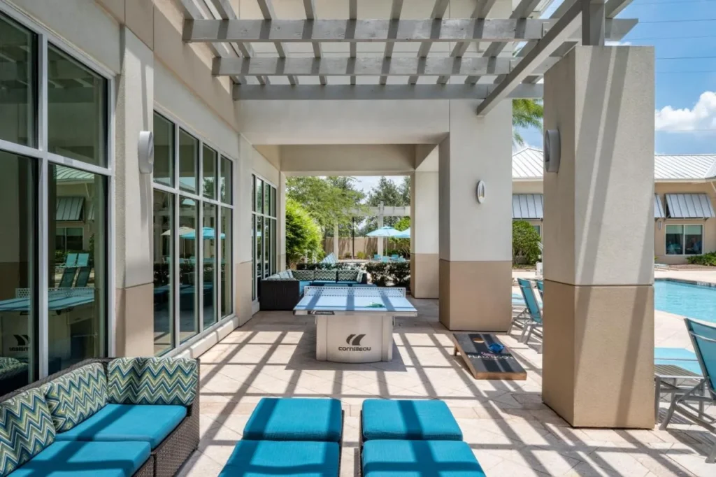 Patio cubierto con mesa de ping-pong, cornhole y tumbonas junto a la piscina en SpringHill Suites Flamingo Crossings