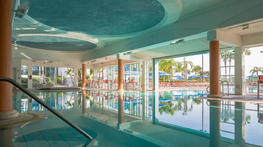Covered pool with columns and glass walls opening onto a sunny palm-lined deck at The Fountains Orlando