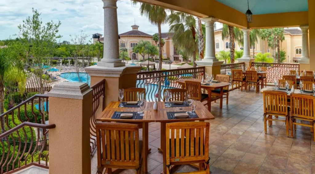 Covered restaurant terrace with wooden tables overlooking the pool and palm trees at Rosen Shingle Creek