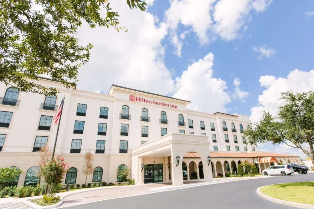 Fachada de estilo mediterr&aacute;neo crema y entrada arqueada de Hilton Garden Inn Winter Park en un d&iacute;a soleado
