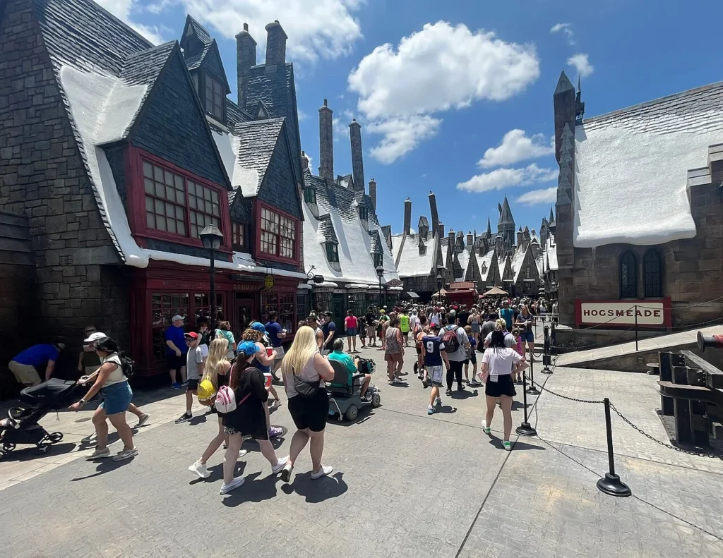 Crowds walking past snow-roofed shops in Hogsmeade at Universal Islands of Adventure on a sunny day