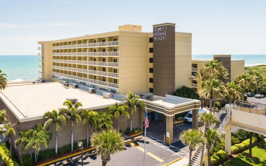 Crowne Plaza Melbourne-Oceanfront entrance, palm trees and eight-story building with the Atlantic behind