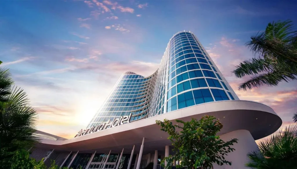 Torre de vidrio curvado y dosel de entrada de Universal Aventura Hotel contra un cielo al atardecer