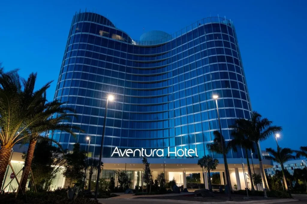 Torre de cristal curvada del Hotel Universal Aventura iluminada al atardecer con su cartel de entrada