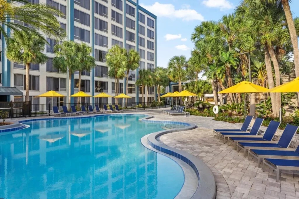 Piscina exterior curvada con tumbonas azules y sombrillas amarillas en Delta Hotels Orlando Celebration