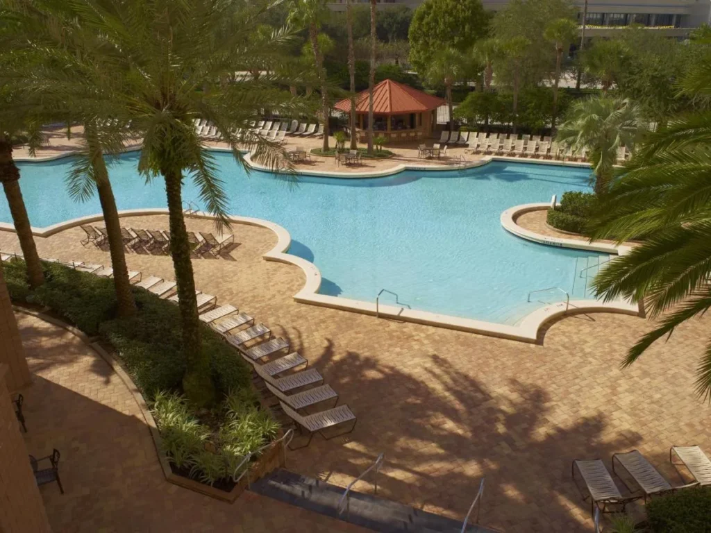 Curved outdoor pool with lounge chairs, palm trees and a red-roofed kiosk at Rosen Centre Hotel