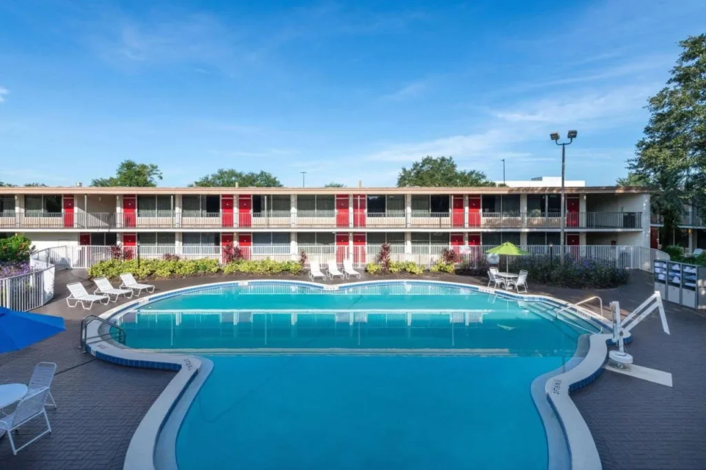 Piscina exterior curva con tumbonas junto a un ala de dos pisos en Ramada by Wyndham Kissimmee Gateway