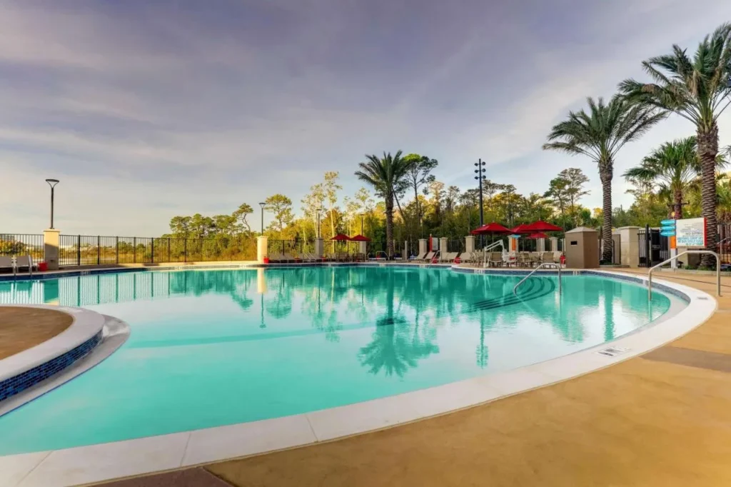 Curved outdoor pool with palm trees and red umbrellas at Drury Plaza Hotel Orlando
