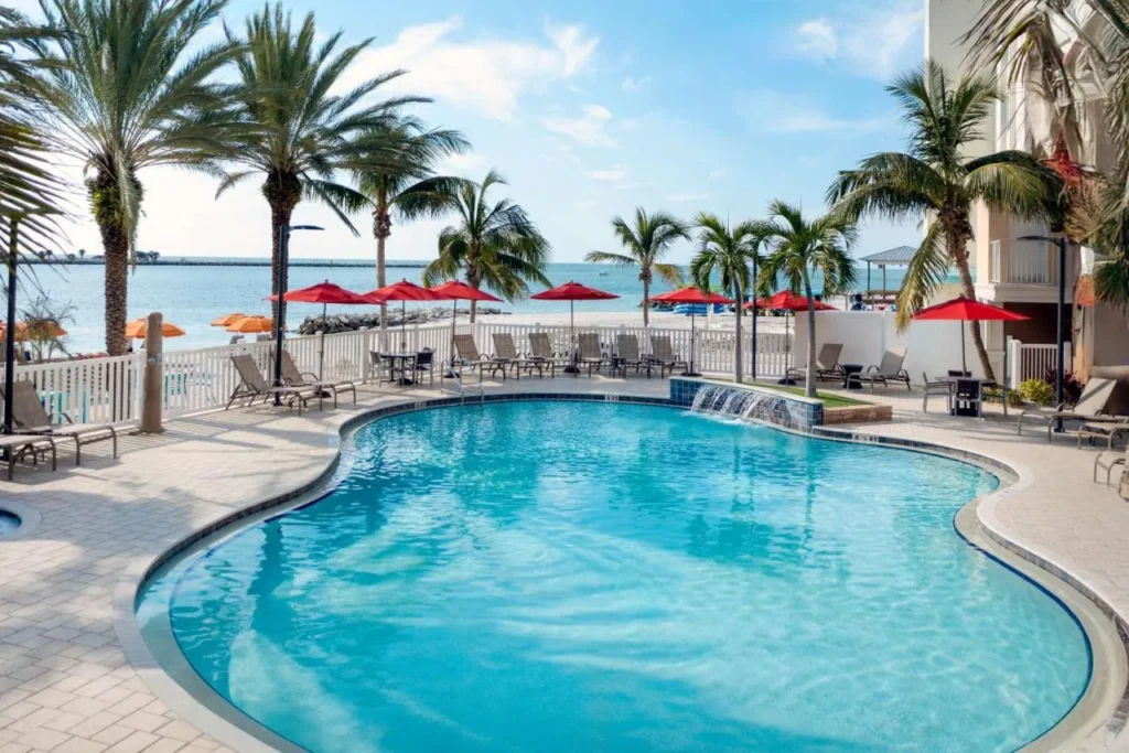 Piscina curva, sombrillas rojas y palmeras junto al agua en Hampton Inn & Suites Clearwater Beach