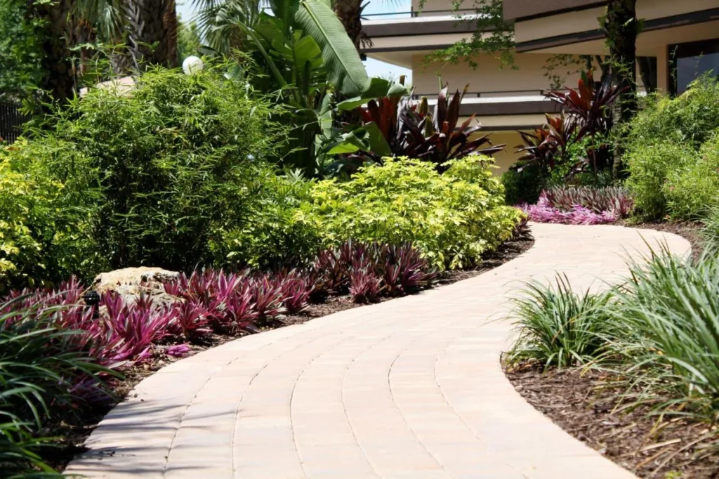 Sendero curvo de adoquines entre plantas tropicales junto a un edificio de habitaciones en Rosen Inn at Pointe Orlando