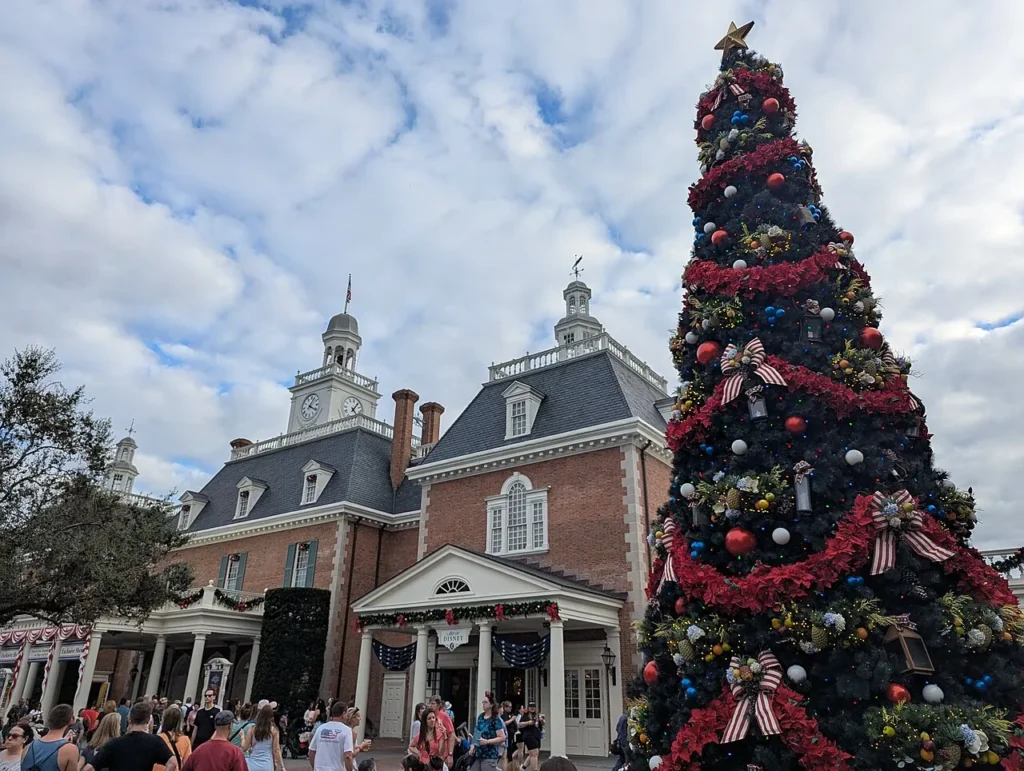 Decorated Christmas tree with red garlands beside the brick American Adventure pavilion in EPCOT's World Showcase