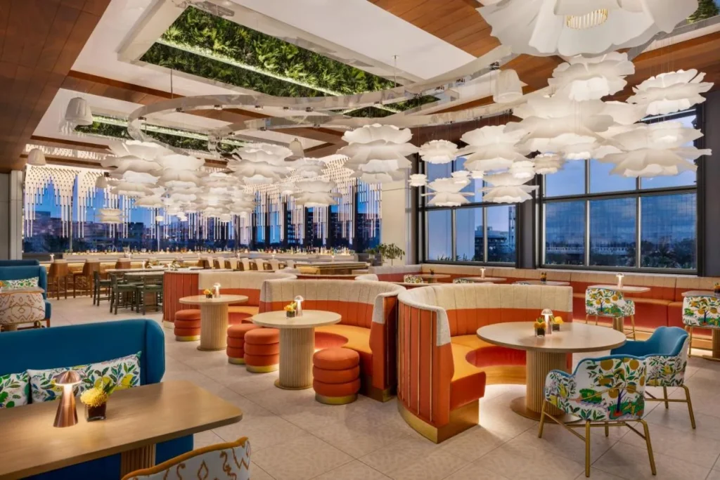 Comedor con cabinas curvas de color naranja, colgantes en forma de flor y ventanas altas en Lake Nona Wave Hotel