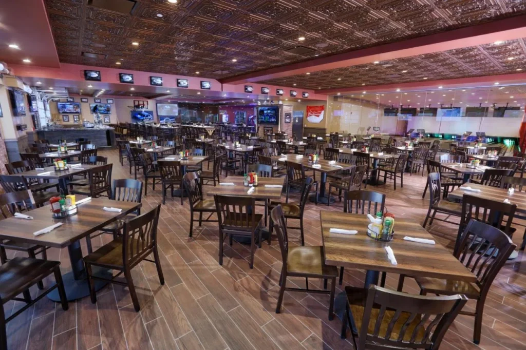 Dining room with wooden tables, sports TVs and bowling lanes behind glass at Drafts, Westgate Lakes