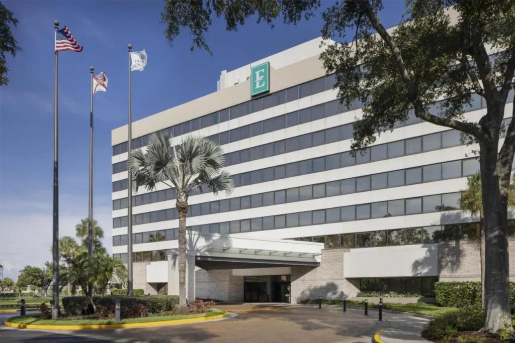 Embassy Suites Orlando International Drive Torre ICON Park con astas de bandera, palmeras y entrada cubierta