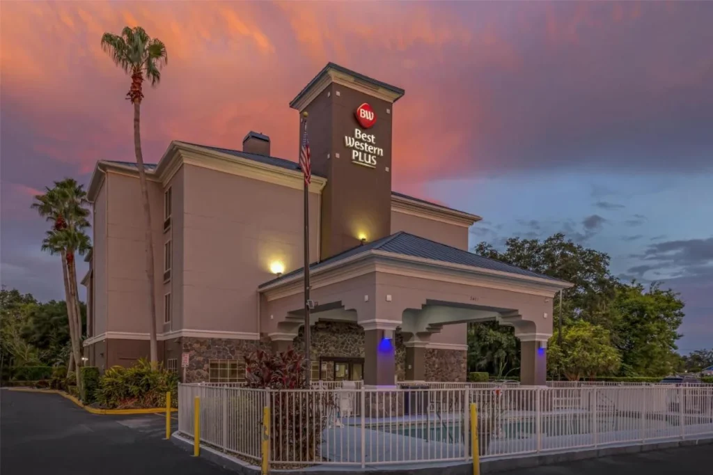 Entrada y torre del Best Western Plus Sanford Airport/Lake Mary Hotel bajo un cielo rosado