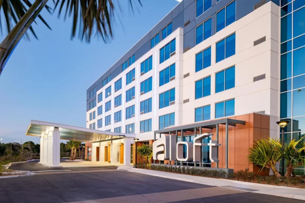 Dosel de entrada y se&ntilde;al en alto del Aloft Orlando Lake Nona con frente de vidrio bajo un cielo despejado