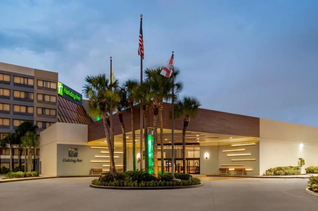 Canopy de entrada, palmeras y astas de bandera al atardecer en el Holiday Inn Orlando International Airport